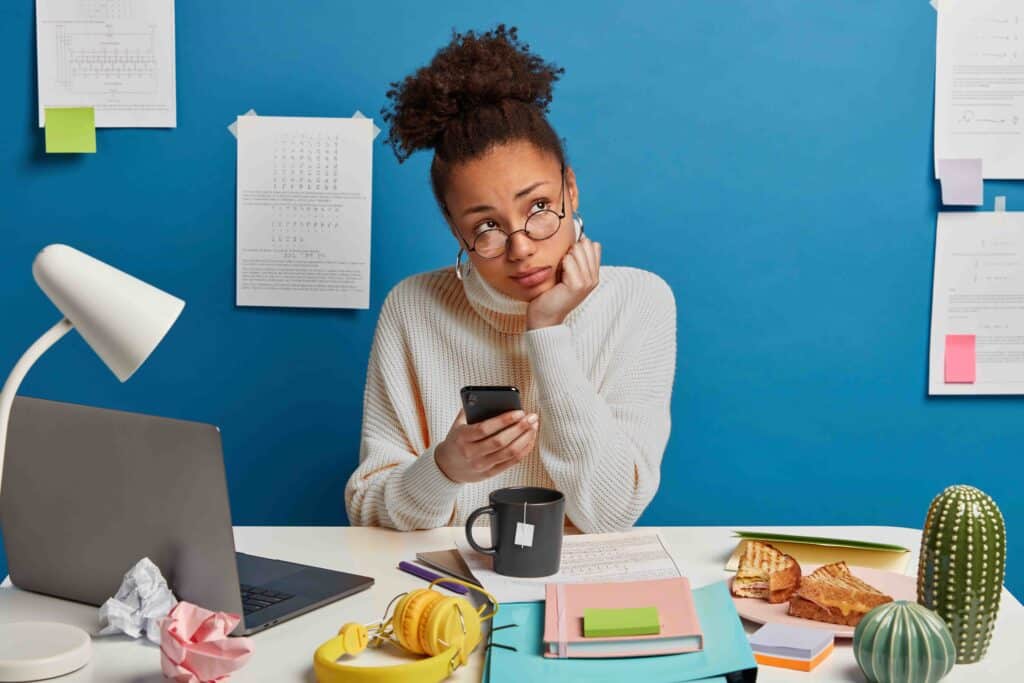 Garota sentada em uma mesa com o celular na mão.